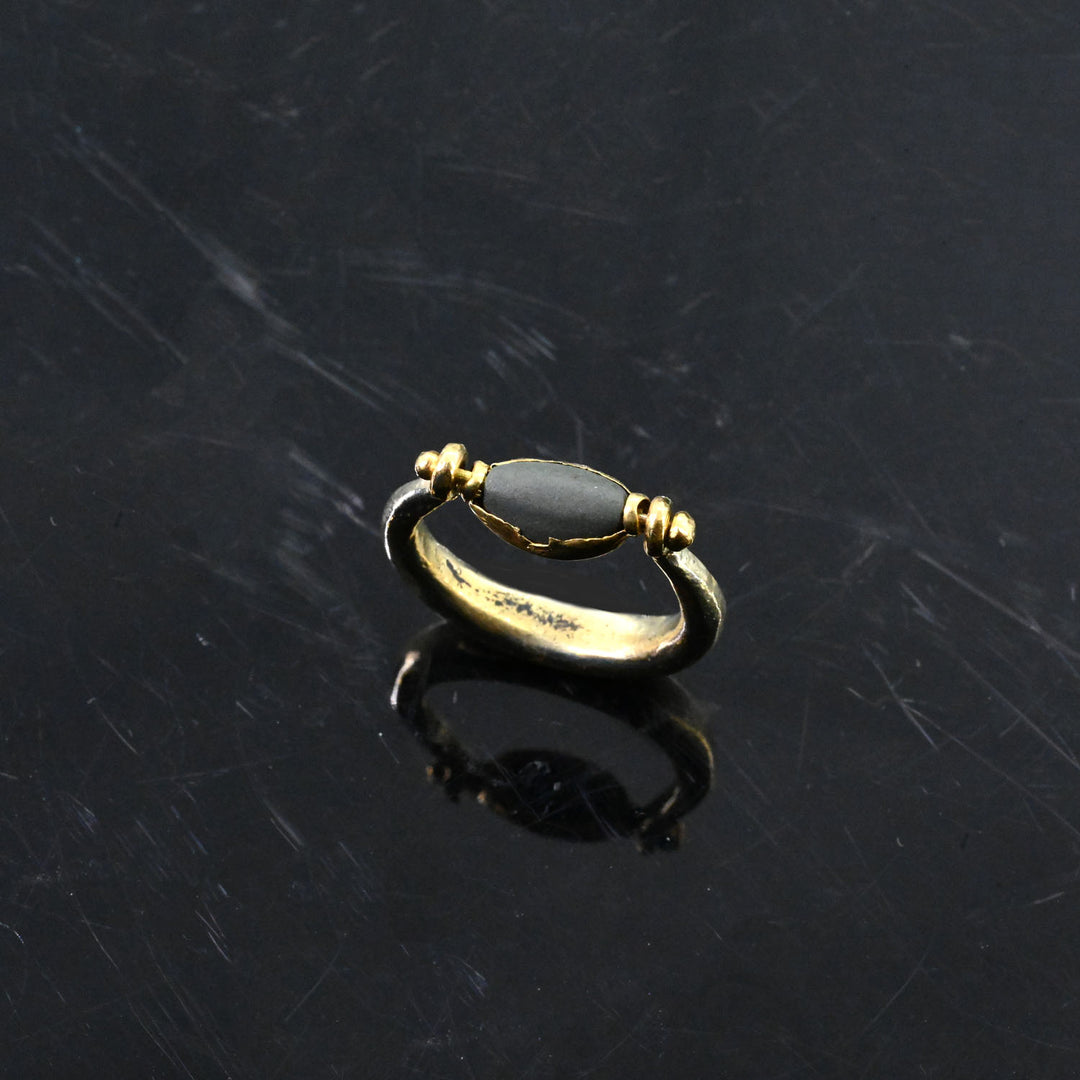 Gold ring with a dark stone on a dark textured surface