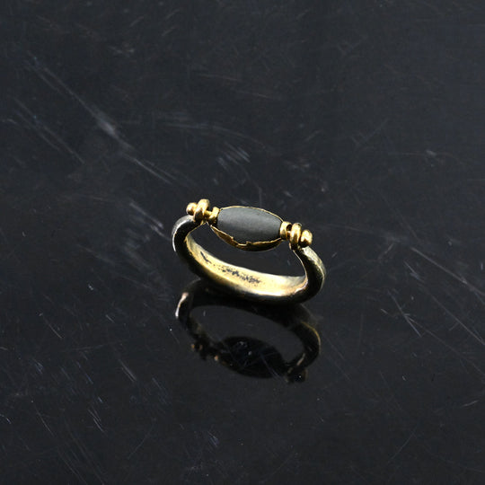 Gold ring with a dark stone on a dark textured surface